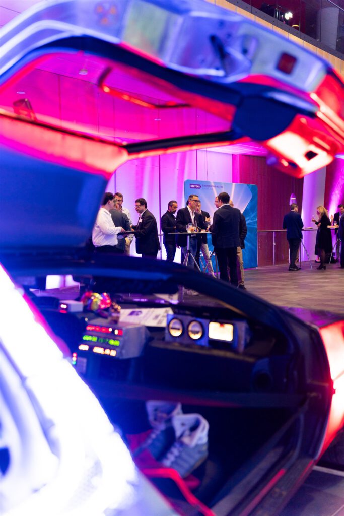 DENTONS Event in München. Farbfotografie. Back to Future Autoim Vordergrund. Im Hintergrund Gäste. Fotografiert von der Eventfotografin Jennifer Hartmann.